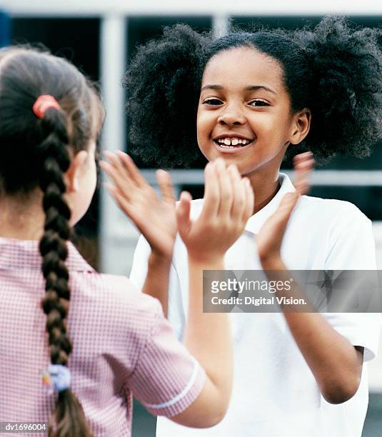 two primary school girls playing patacake face to face in the playground - only girls stock pictures, royalty-free photos & images