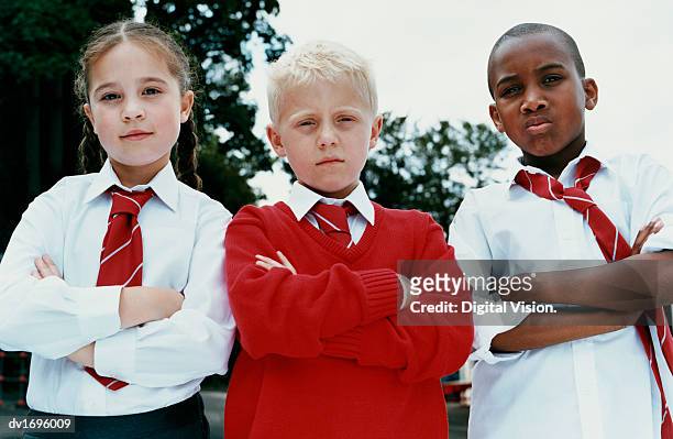 portrait of three primary school children standing with their arms folded, scowling at the camera - school uniform stock pictures, royalty-free photos & images