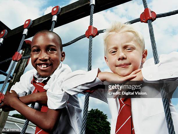 two primary school boys lean on a climbing frame and smile at the camera - school tie stock-fotos und bilder