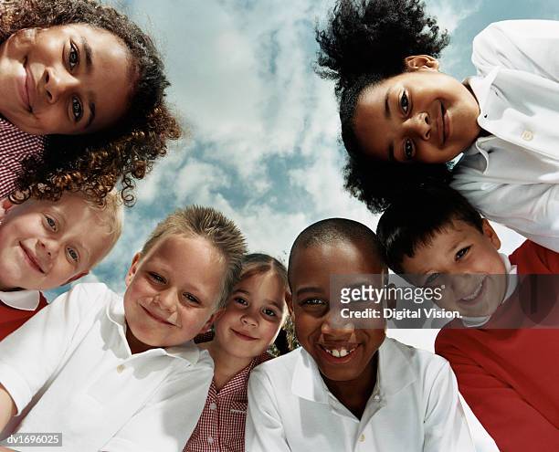 view directly below of seven primary school children huddled together looking at the camera - niño de primaria fotografías e imágenes de stock