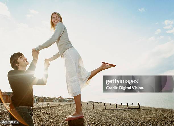 man holding hands with a woman as she balances on a breakwater post on a pebble beach - voyage15 photos et images de collection