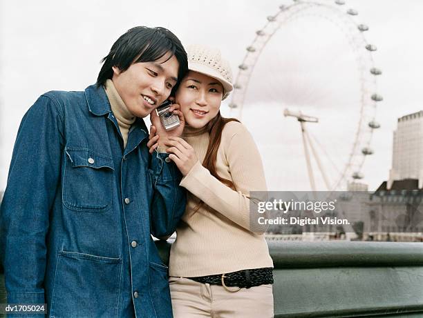 young couple stand side by side, listening to their mobile phone, the millenium wheel in the background, london - vigils are held for the victims of the london bridge terror attacks stockfoto's en -beelden