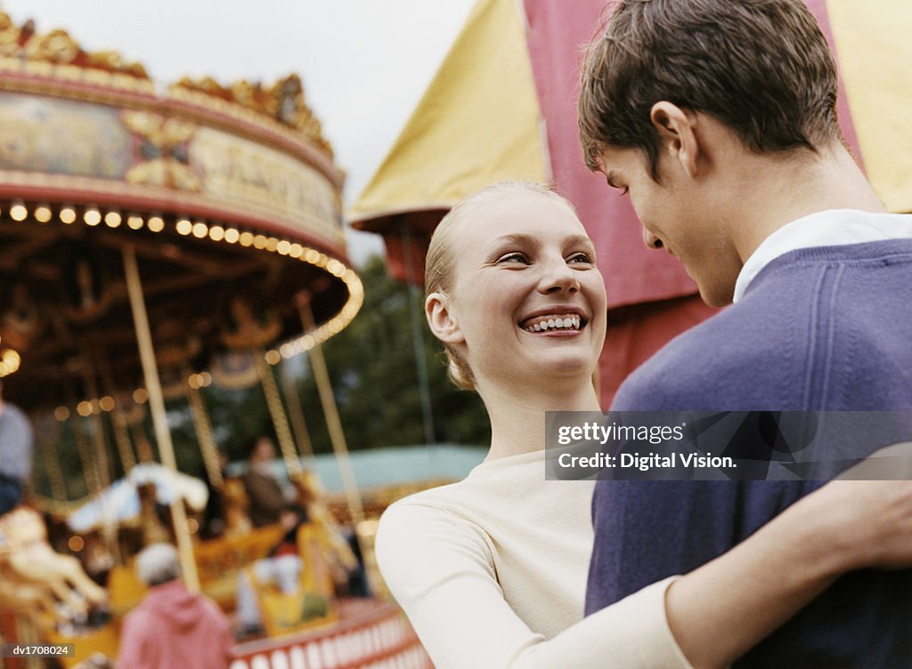 Teenage Couple Stand in a Fairground Laughing and Embracing