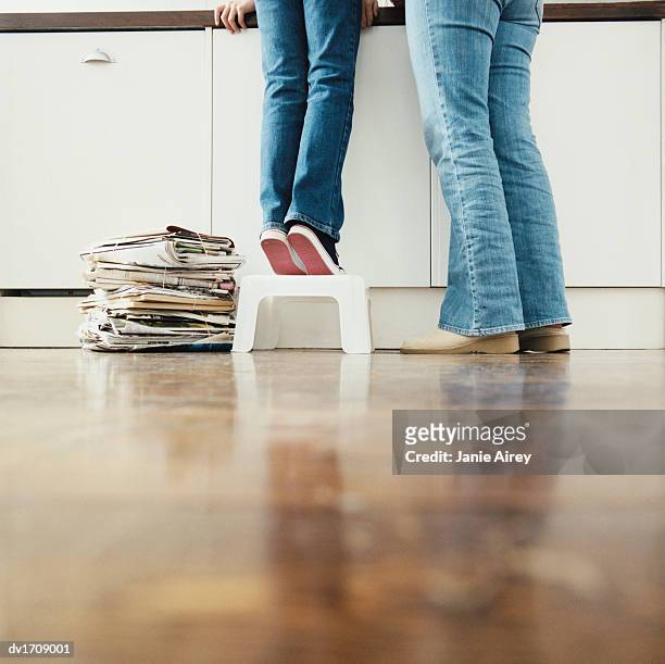 low section of a mother with her child standing in a kitchen, child standing on a step stool next to a tied up bundle of newspaper - step stool imagens e fotografias de stock