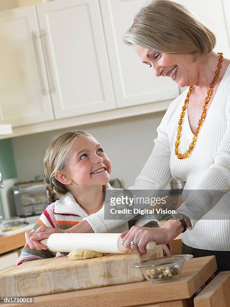 granddaughter gazing at her grandmother as she uses a rolling pin - pin up girl stockfoto's en -beelden