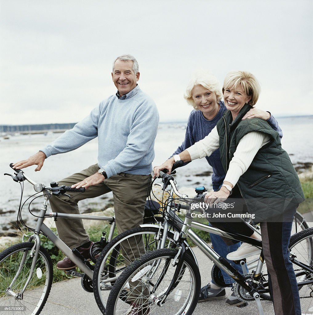 Senior Couple and a Friend Sitting on Bikes on the Coast