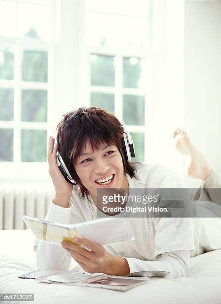 young man lying on a bed listening to music on headphones and holding a cd box - music box stock pictures, royalty-free photos & images