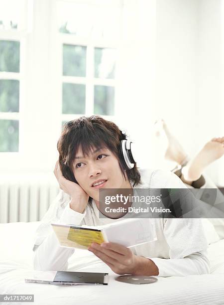 young man lying on a bed and listening to music on headphones - music box 個照片及圖片檔