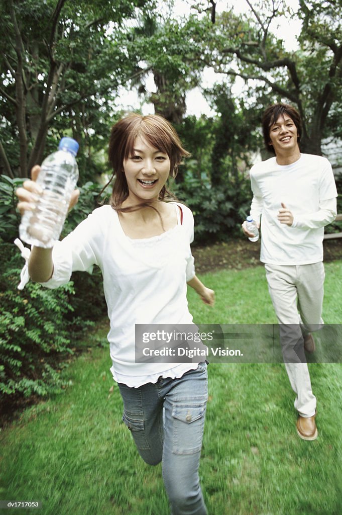 Man and Woman Running Outdoors, Woman Holding a Water Bottle