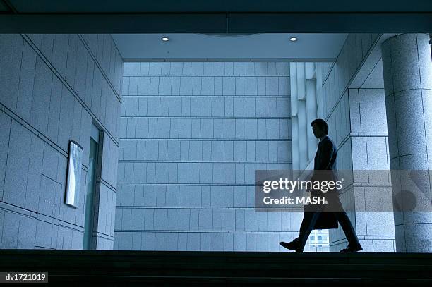 businessman in silhouette walking past a stone wall - walking past office wall stock pictures, royalty-free photos & images