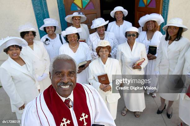 elevated view of smiling priest standing in front of a congregation outside a church holding a bible - clérigo fotografías e imágenes de stock