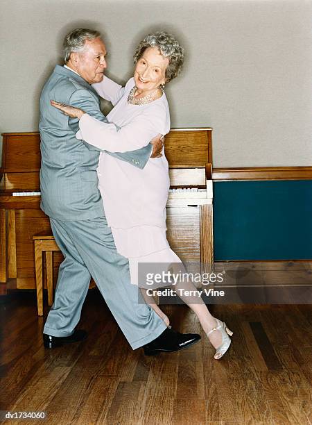 portrait of a senior couple dancing in a room with wooden flooring and a piano in the background - ballroom dance couple stock-fotos und bilder