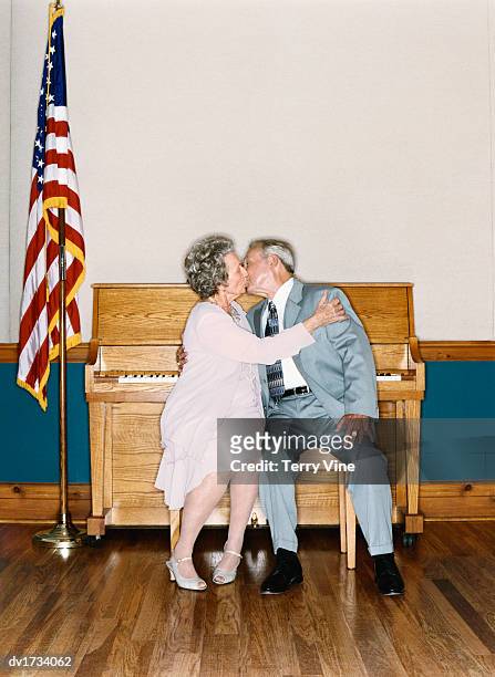 senior couple sitting on a stool, kissing, in a room containing a piano and the stars and stripes - lionsgate uk screening of film stars dont die in liverpool after party stockfoto's en -beelden