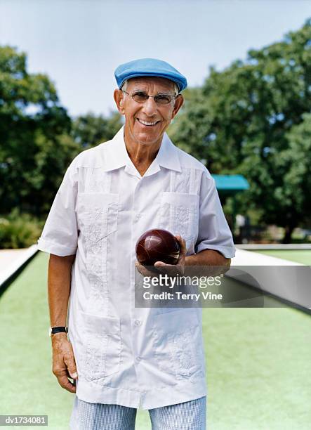 smiling senior man standing on bowling green holding a bowling ball - bowls stock-fotos und bilder
