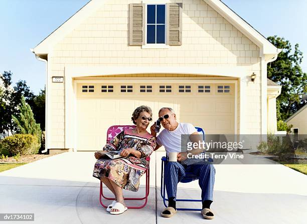 senior couple sit on chairs outside their house listening to a mobile phone - funny slipper stock pictures, royalty-free photos & images