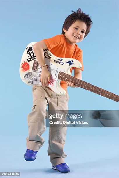 smiling young boy stand on one leg holding a heavy electric guitar - guitar stand stock pictures, royalty-free photos & images