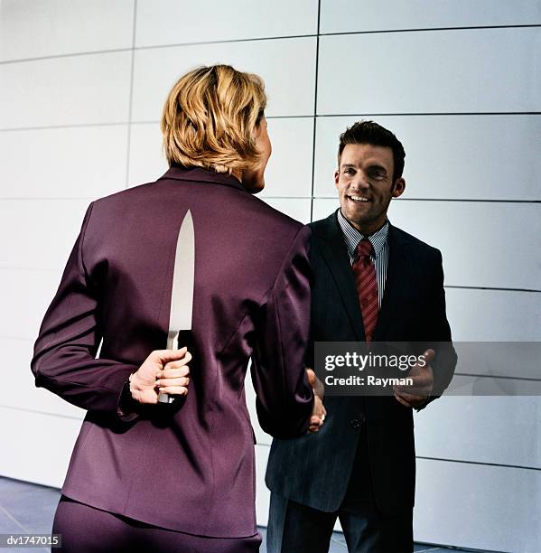 businesswoman holding a knife behind her back greets a businessman - puñalada por la espalda fotografías e imágenes de stock