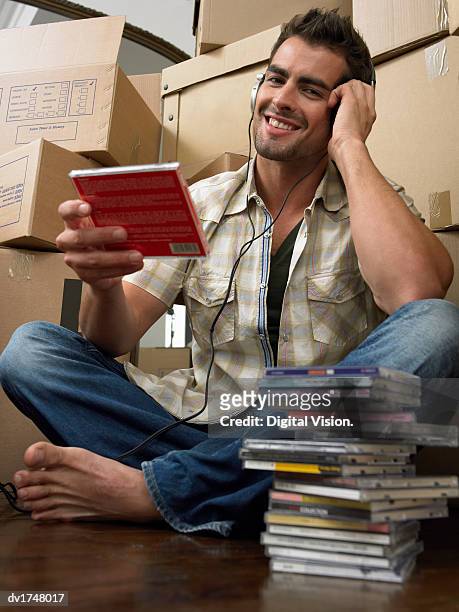 man moving into a new home, sitting cross-legged, listening to music on a personal stereo - personal stereo stockfoto's en -beelden