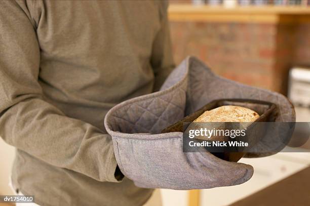 unrecognizable person wearing oven gloves and holding a baking tray with a freshly baked loaf inside - loaf stock pictures, royalty-free photos & images