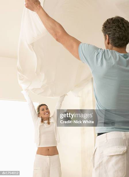 couple with their arms in the air holding up a clean bed sheet - air date stockfoto's en -beelden