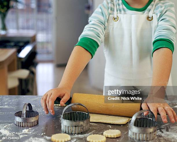 mid section of a child standing by a kitchen counter using a rolling pin and pastry cutters to prepare pastry - rolling pin photos et images de collection