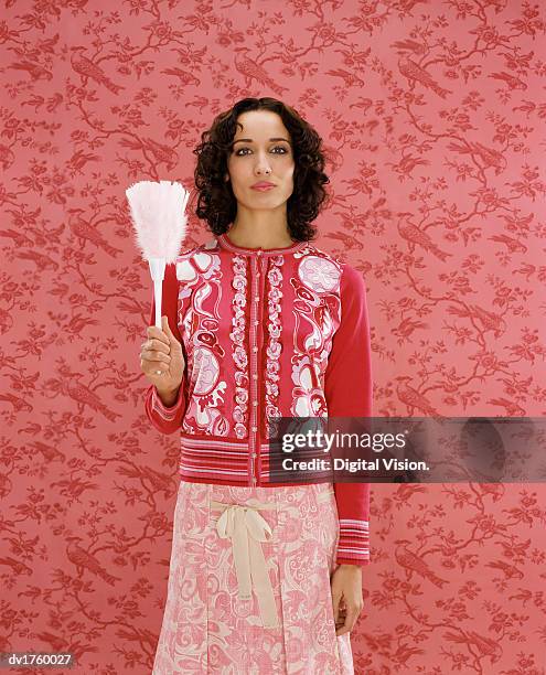 portrait of a woman standing holding a feather duster - vrouw behangen stockfoto's en -beelden