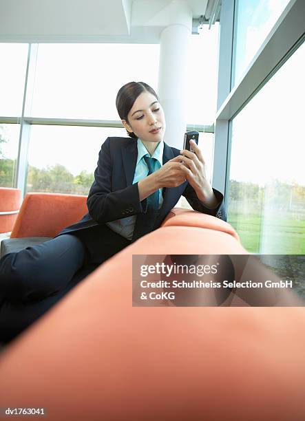 businesswoman wearing a full suit sitting on a sofa and dialing a mobile phone - full suit ストックフォトと画像