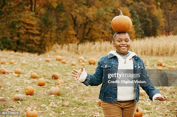 smiling young girl balancing a pumpkin on her head - chubby girls stock pictures, royalty-free photos & images