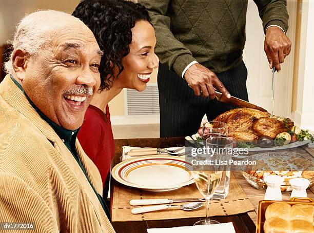 father and daughter sitting at a dining table as a man slices a roast turkey for thanksgiving dinner - carving knife imagens e fotografias de stock