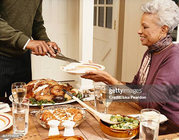 man serving a slice of roast turkey to a mature woman sitting and lifting a plate - carving set stock pictures, royalty-free photos & images