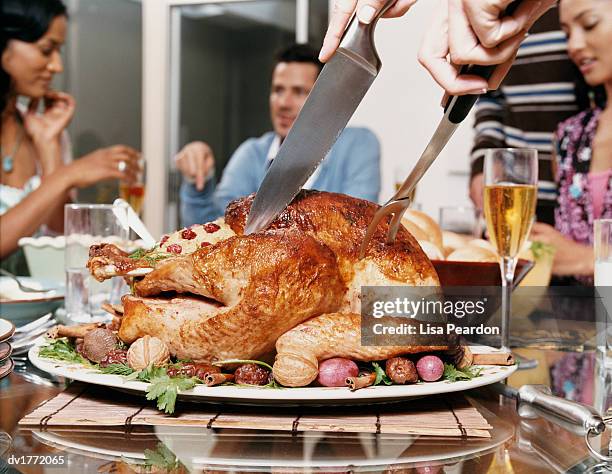 small group of friends sit round a dining table while a thanksgiving turkey is cut - carvery stock pictures, royalty-free photos & images