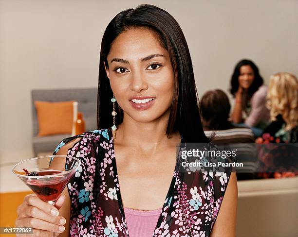 woman stands holding a cocktail glass while her friends sit in the background - adult cocktail party background stock-fotos und bilder