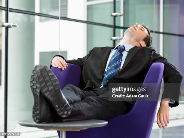 exhausted businessman sleeps on an armchair with his feet up on a coffee table - adam slack stock pictures, royalty-free photos & images