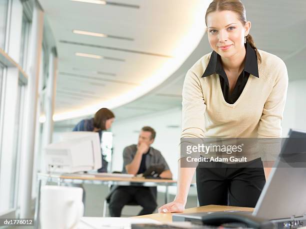 businesswoman leaning on a table in an open plan office and people working in the background - open collar stock-fotos und bilder