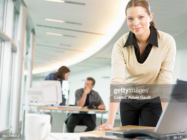 businesswoman leaning on a table in an open plan office and people working in the background - open collar foto e immagini stock