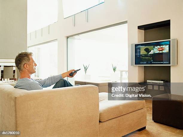 mature man sits watching tv in a modern home interior - one mature man only foto e immagini stock