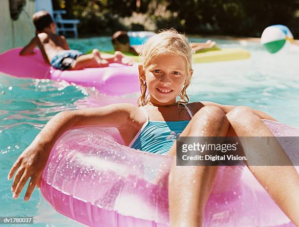 smiling girl sits in a rubber ring in a swimming pool - rubber ring stock-fotos und bilder