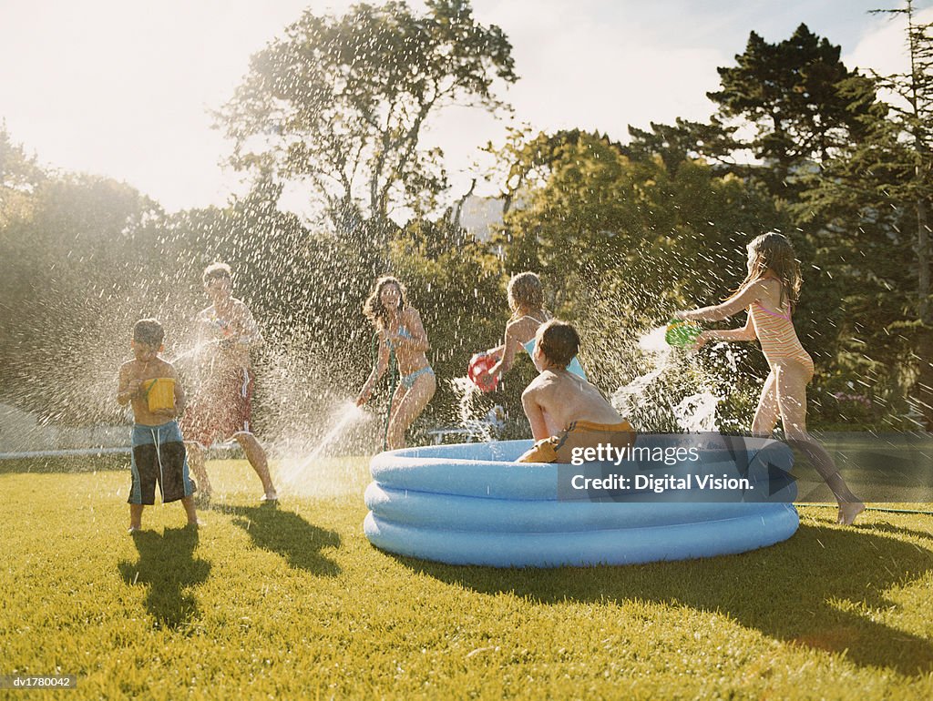 Six Children Have a Water Fight Round a Paddling Pool in a Back Garden