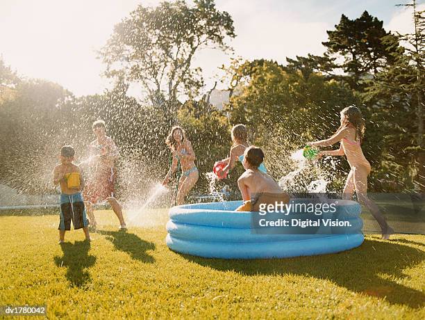 six children have a water fight round a paddling pool in a back garden - paddling pool stock pictures, royalty-free photos & images