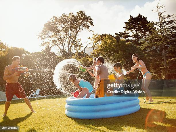 father aims a water gun at children throwing water in a paddling pool - family pool stock-fotos und bilder