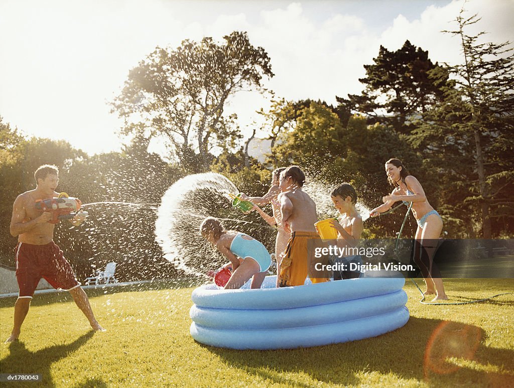 Father Aims a Water Gun at Children Throwing Water in a Paddling Pool