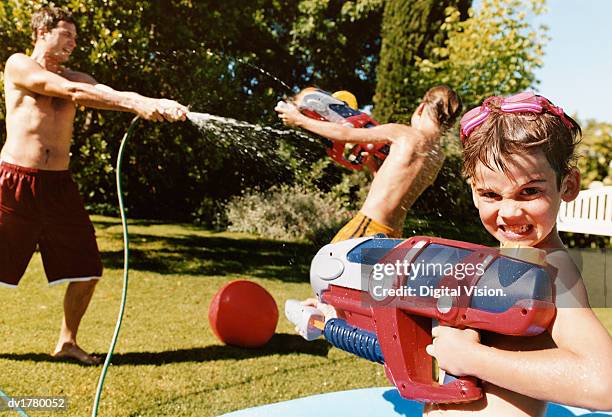 young boy stands with a water pistol as his father sprays water from a hose - two kids playing with hose stock pictures, royalty-free photos & images