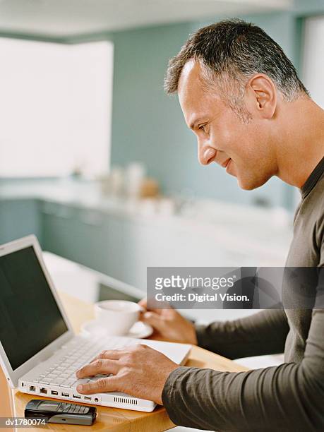 man uses his laptop at his kitchen table - uses stock pictures, royalty-free photos & images