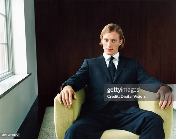 portrait of a young, confident man in a black suit sitting in an armchair by a window - well dressed young man stock pictures, royalty-free photos & images