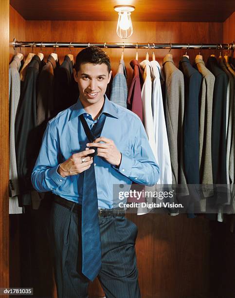 young man stands in front of a line of jackets doing-up his tie - untied stock pictures, royalty-free photos & images