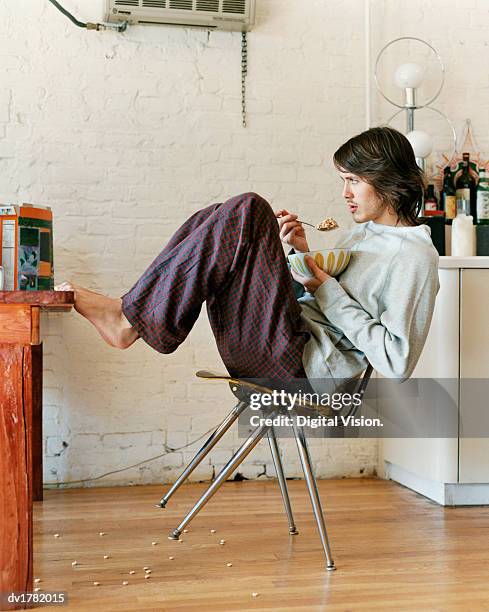 bachelor in a kitchen leaning back on a chair and eating breakfast cereal - 20 20 vision bildbanksfoton och bilder