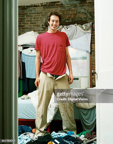 young man standing in a messy bedroom in an apartment - bachelor apartment stock pictures, royalty-free photos & images