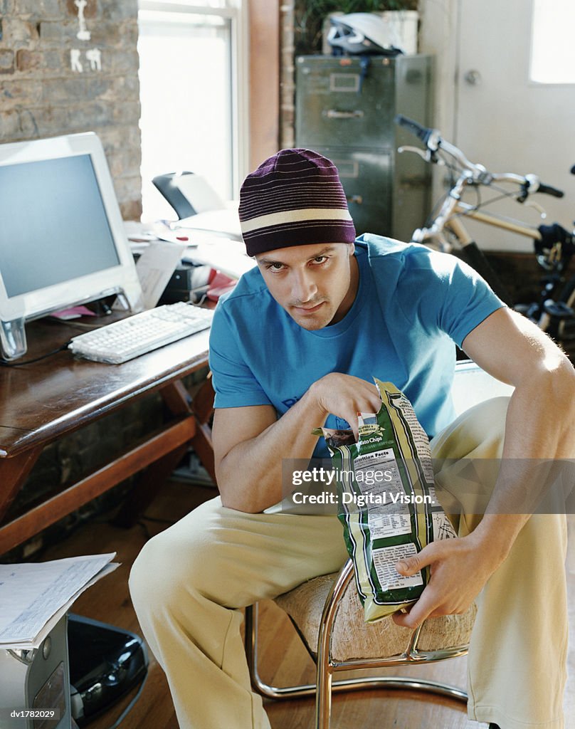 Thirty something Man Sitting on a Chair in an Apartment Looking Serious and Eating Crisps