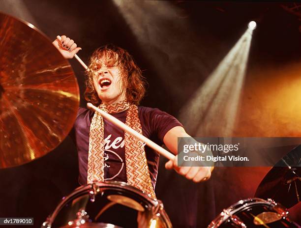 drummer in a rock band performs on a spot lit stage, hitting the cymbal of his drum kit and shouting - rock band shirt stock pictures, royalty-free photos & images