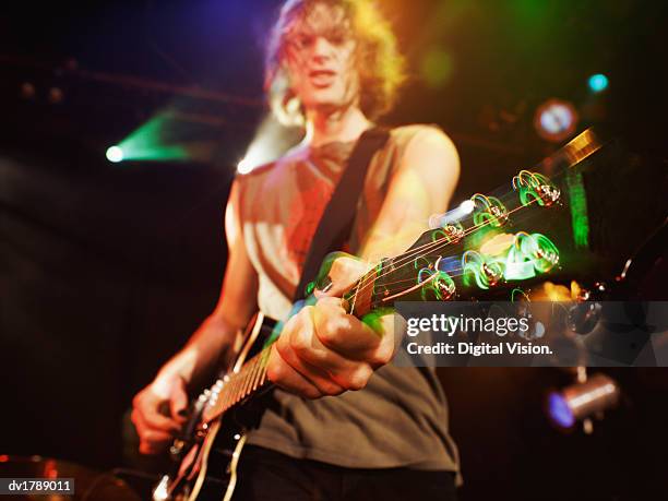 low angle view of a rock musician playing a guitar on stage, focus on the foreground - modern rock stock pictures, royalty-free photos & images